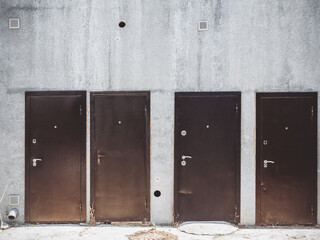 Four iron brown doors located outside on the wall of a gray concrete building