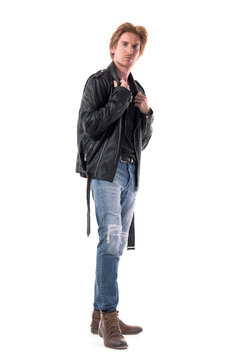 Side view of confident young man in jeans and boots adjusting black leather jacket. Full body length isolated on white background. 