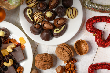 sweet food background for christmas or holiday decoration - chocolate candies, tangerines, nuts and dried fruits on white wood
