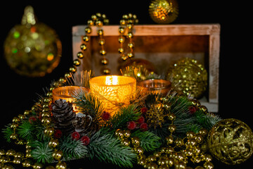 Christmas decorations on a black background by candlelight. Composition of Golden balls and beads, openwork candlesticks with patterns and branches of the Christmas tree. Elegant cones and red berries