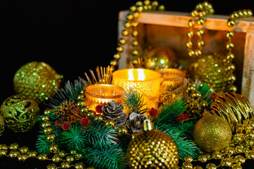Obraz na płótnie Canvas Christmas decorations on a black background by candlelight. Composition of Golden balls and beads, openwork candlesticks with patterns and branches of the Christmas tree. Elegant cones and red berries