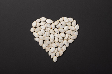 Delicious salted pumpkin seeds in the shape of a heart on a dark background. The concept of a favorite and healthy food.