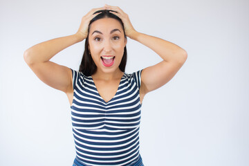 Close up portrait of young beautiful woman wearing striped t-shirt surprised with arms on head over white background.