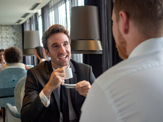 Image of young businessman with cup of coffee communicating with colleague
