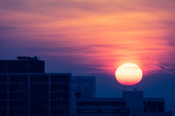 large round orange sunrise with cloudy sky over city for background, image shot with super telephoto lens