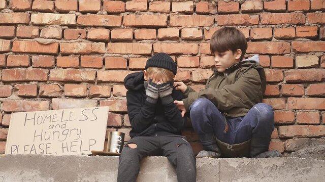 Depressed street boy sit crying while his friend calm down and support him, need food.
