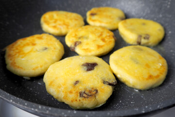 seven yellow curd cheesecakes without sugar in corn flour, fried in coconut oil in a gray pan side view . cooking gluten-free cheesecakes at home