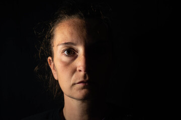 Dark portrait of a serious woman with only half face illuminated on black background. Feelings of...