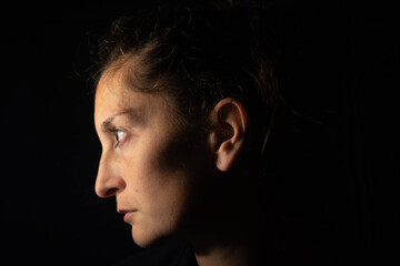 Dark profile portrait of a very dimly lit woman. The woman is looking straight ahead and transmits...