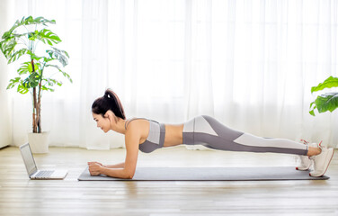 Young  woman in sportswear watching online video with fitness exercises on laptop