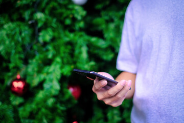Man holding smartphone with christmas tree background, Technology concept.