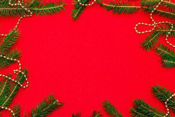 Fototapeta na wymiar Christmas background with fresh Xmas tree branches and New Year gold beads on red background