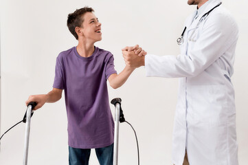 Cropped shot of male doctor shaking hands with cheerful disabled boy with cerebral palsy, taking steps using his walker isolated over white background