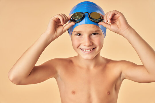 Joyful boy swimmer standing against light orange background
