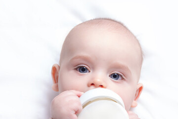 Caucasian baby boy with baby milk bottle on white blanket. Close up. Baby feeding and artificial nutrition concept.