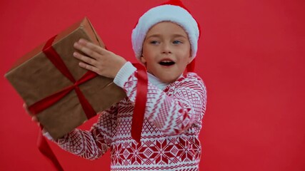excited girl in santa hat and christmas sweater shaking gift box isolated on red - Powered by Adobe