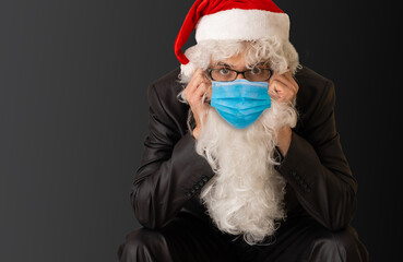 Real Santa Claus on background, wearing protective mask and with an open hand in front making a pandemic stop sign. Christmas with social distance. Covid-19