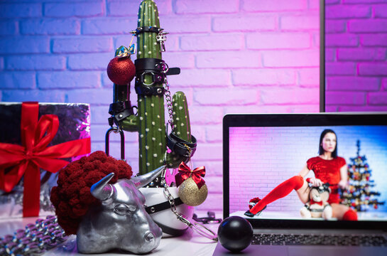 cactus dressed up In accessories for BDSM games on the Christmas table with gifts next to the TV with the image of a girl in a red bodysuit