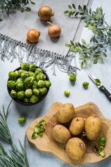 Flat lay Brussels sprouts in bowl, potatoes on wooden plate  and onions