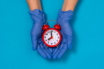 Hands in medical gloves holding red alarm clock