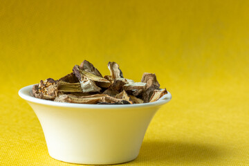a bunch of dried porcini mushrooms, in a white saucer on a yellow background with a shadow pattern