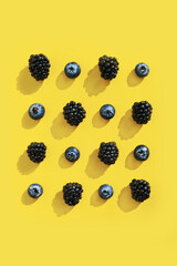 Blackberries and Blueberries isolated on Illuminating yellow background. Trendy Color of th year 2021.