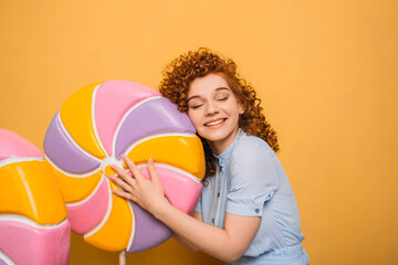 Lollipop, I love you. Very happy red-haired woman hugging lollipop candy, on orange background