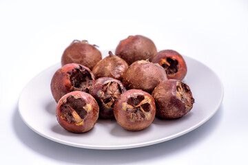 Fresh ripe organic common medlar fruit on a plate on white background. Healthy food Mespilus germanica