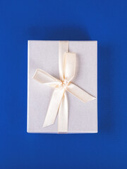 The beautiful new year composition of the packed present with the white satin ribbon on the blue background.