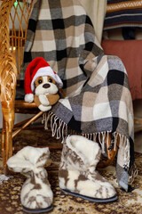 toy in a Santa hat on a wicker chair. Next to a checkered plaid and fur boots
