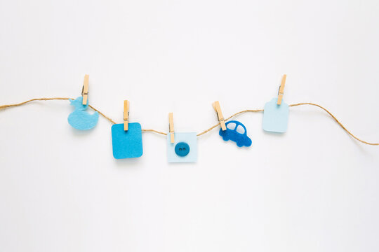 Baby Boy Concept. Blue Decor And Toys Are Hung On Rope On White Background. Newborn Accessories. Children's Background, Invitation Or Greeting Card Idea, Copy Space.