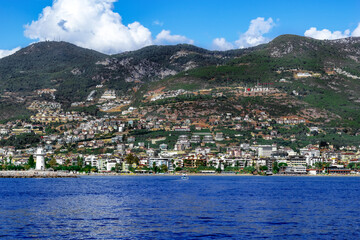 Fototapeta na wymiar Alanya (Turkey) coastline panorama - view from Mediterranean Sea. I love Alanya sign on the hillside and a lighthouse in the water against the background of a modern tourist town among the mountains
