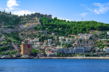 Fototapeta premium Kizil Kule Tower and Alanya Old Town on the hillside - view from the sea. Panorama of Turkish tourist town on a summer sunny day