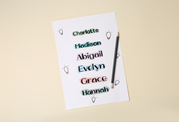 List of different baby names and pencil on beige background, top view