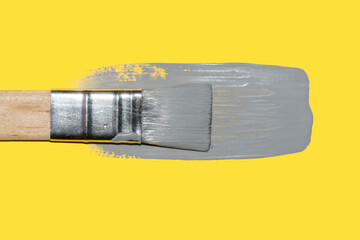 paint brush with fresh ultimate gray paint on illuminating yellow background