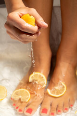 Woman's feet in lemon bath soaking and hand squeezing lemon.