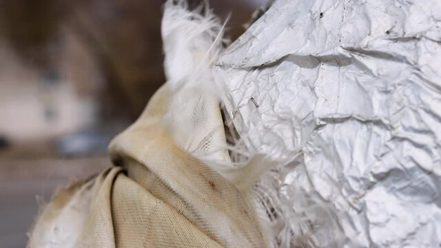 Close-up shot of torn, damaged insulation on water pipes blowing in the wind in the city with cars moving in the background. Problems with communications in the city. Engels. Saratov region. Russia.