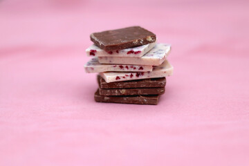 Stack of dark and white chocolate pieces. Selective focus, pink background.