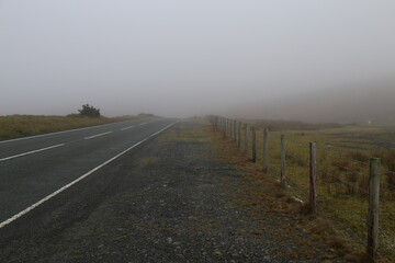 A foggy road leading down a hill through farmland in remote Wales, UK.