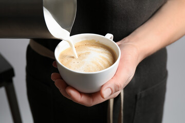 Woman pouring milk into cup of coffee on grey background, closeup