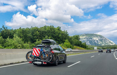 Black car with roof luggage box and trunk bike rack driving on highway. Beautiful mountain...