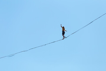 A man walks along the highline against the blue sky.