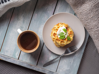 Light breakfast with zucchini waffles and coffee in beige ceramic dishes on a wooden tray