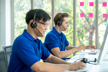 Customer service agent working in call center in modern worldwide office he talking and looking on screen of desktop computer at office.