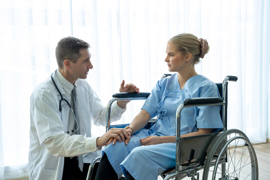 Doctor talks to the patient sitting in the wheelchair at hospital.