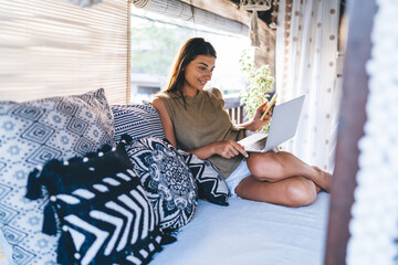 Woman with smartphone in hand using laptop