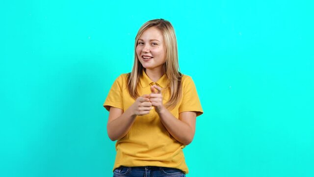 The successful young woman applauds her office colleagues for her success. Beautiful Caucasian woman in yellow t-shirt and long blond hair standing on blue background. A fat teenager. Advertising