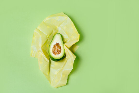 Organic fabric covers for food storage. Reusable Beeswax Food Wraps with half of avocado on green background.