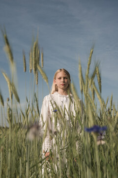 Blonde girl in white dress standing in a field of wheat and grain