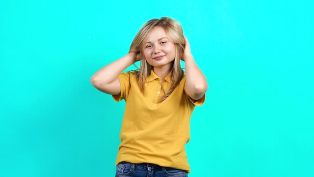 The beautiful young woman who appreciates her beautiful hair. Beautiful Caucasian woman in yellow t-shirt and long blond hair standing on blue background. A fat teenager. Advertising concept.